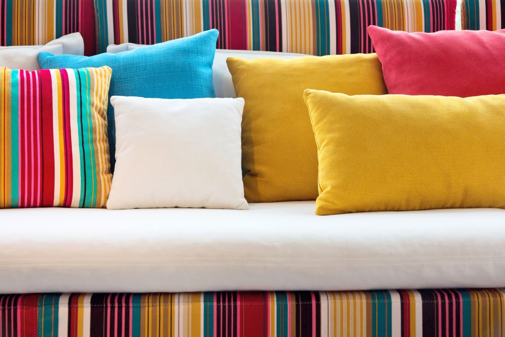 Bright colourful designer cushion covers on a very bright sofa with lines