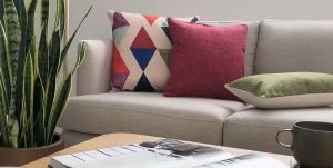 Beige sofa with large patterned couch cushions and a smaller red design with a rectangle green cushion cover laying flat in maroon, red and green arranged on its left side.