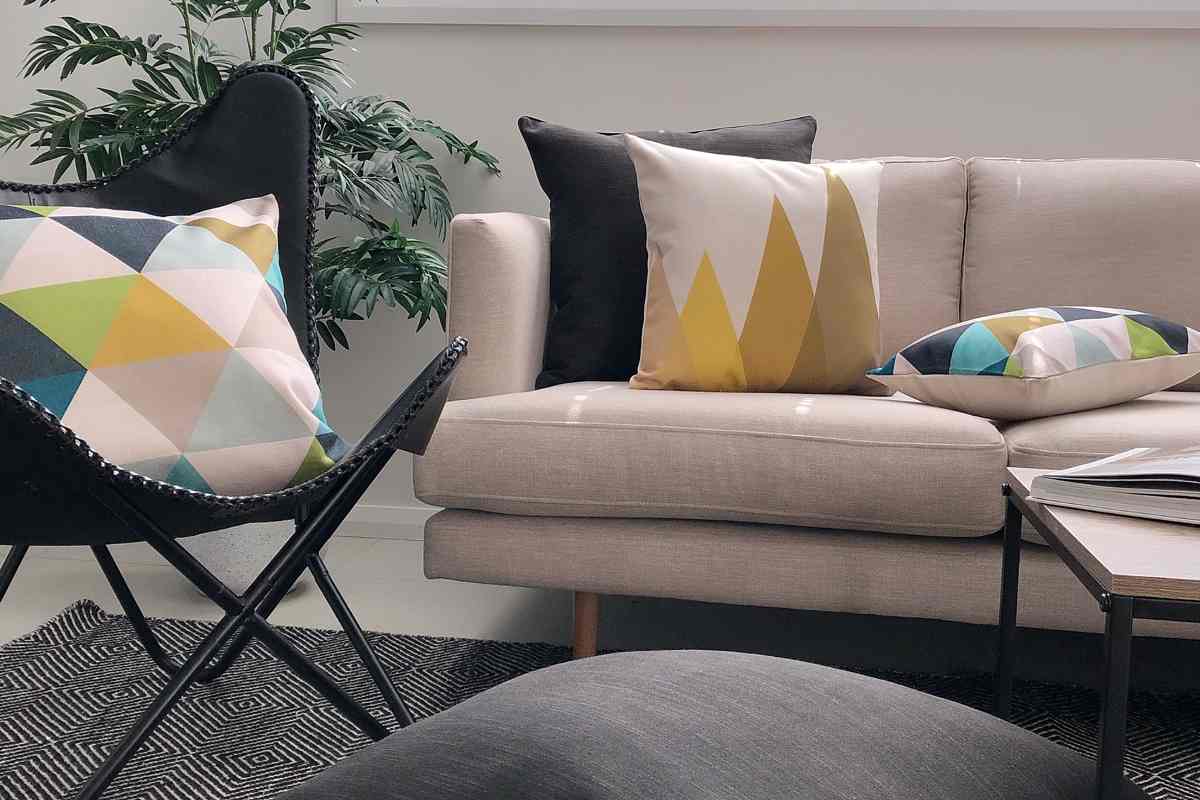 A lounge room scene showing a beige sofa with a dark grey leather arm chair and the Bronte cushion collection