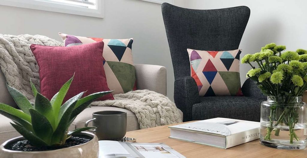 Beautiful photo showing a foreground of a plant and items on a coffee table with mid century modern styled scene in the background including a beige sofa and bright cushions