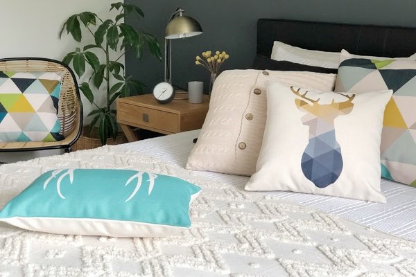Bedroom scene with a range of cushions organised on a bed in teal and blue and cream colours