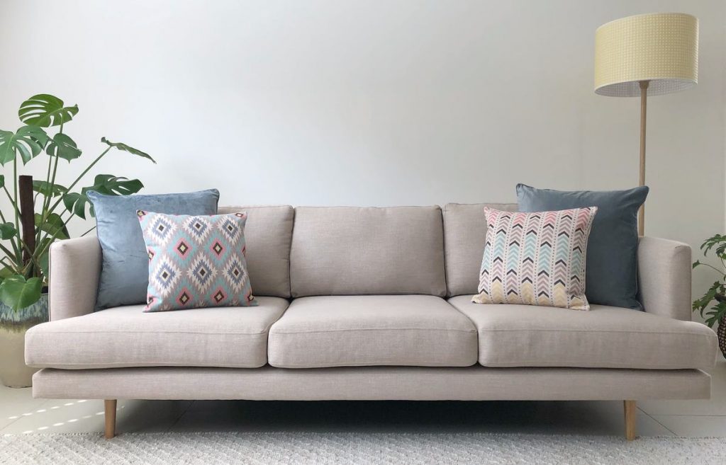 Beige sofa with two large solid grey cushion covers and two smaller print cushion in pastel colours