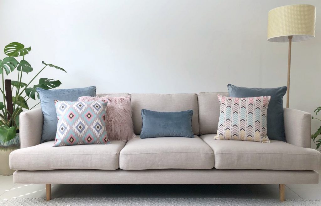 Neutral sofa with blue and grey pastel cushions and a grey velvet rectangular cushion in the centre