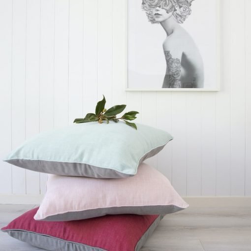 A stack of Albany floor cushions is shown against a white wooden backdrop. Pick, red and teal styles are shown.