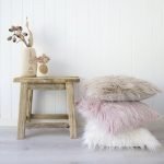 A light coloured room is shown with a stack of faux fur cushions arranged next to a wooden table.