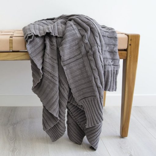 Dark grey throw blanket with fine embroidery sat above a wooden chair