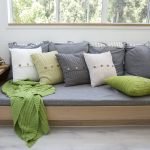 A modern grey sofa exhibits a collection of knit cushions arranged in a sequential style.