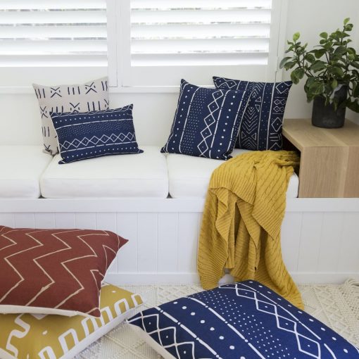 A bright and bold collection of mud cloth style cushions are artfully arranged on a light bench seat with a mustard throw visible.