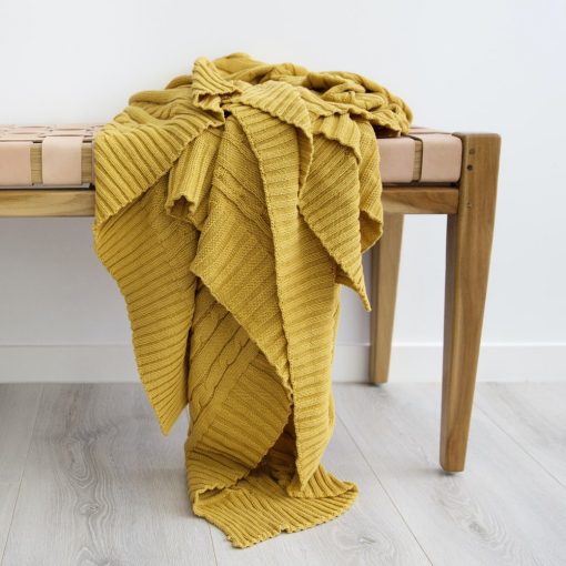 Lush mustard throw blanket folded on a bench seat and displaying a soft cotton weave