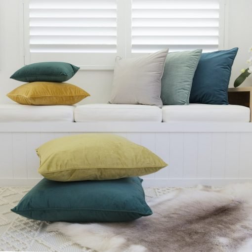 Large velvet cushions adorn a seat while large floor cushions also in a sot velvet material lay in the ground in front.