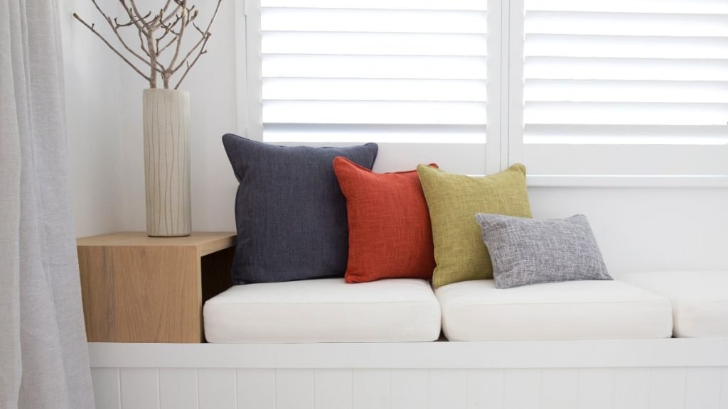 Bold bright block coloured cushions laying in arrangement upon a white seat. They show how to match cushions to sofa colours that are white or neutral.