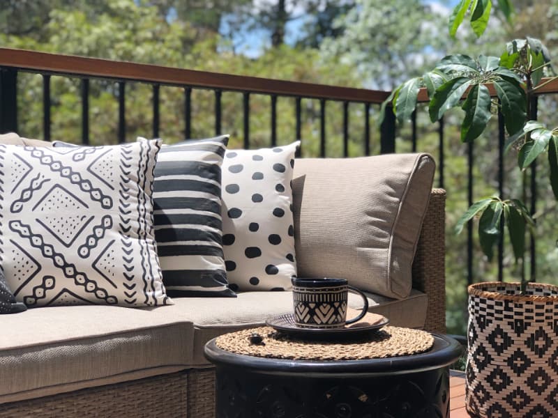 Black and white outdoor cushions with tribal patterns are arranged at the end of a couch with a potted plant in the foreground