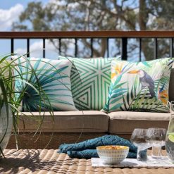 A tropical collection featuring green outdoor cushions lay on an outdoor lounge with a plate of drinks and snacks nearby