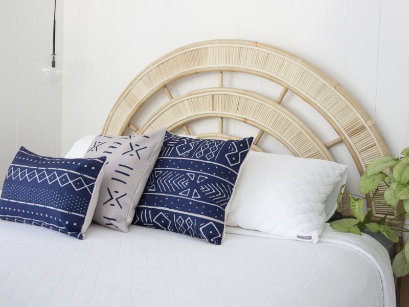 A collection of three blue cushions arranged on a light coloured bed with a wooden bedhead in the background