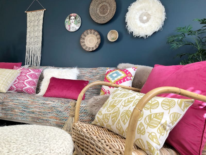 A textured grey couch is shown with a collection of boho pillows layered across it with a number of hot pink cushions standing out