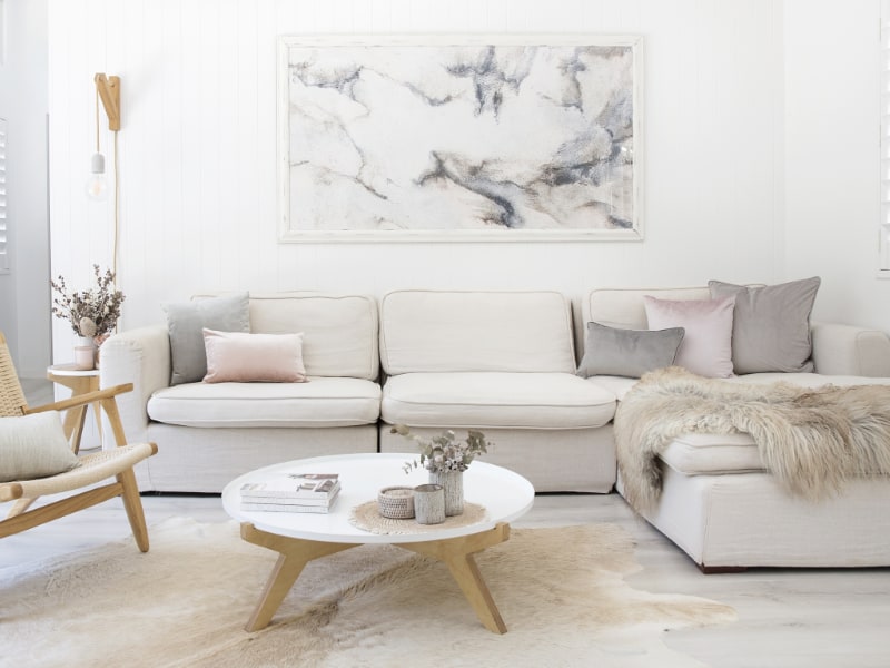 A modern living room scene is shown with grey and blush cushions styled on a light coloured sofa