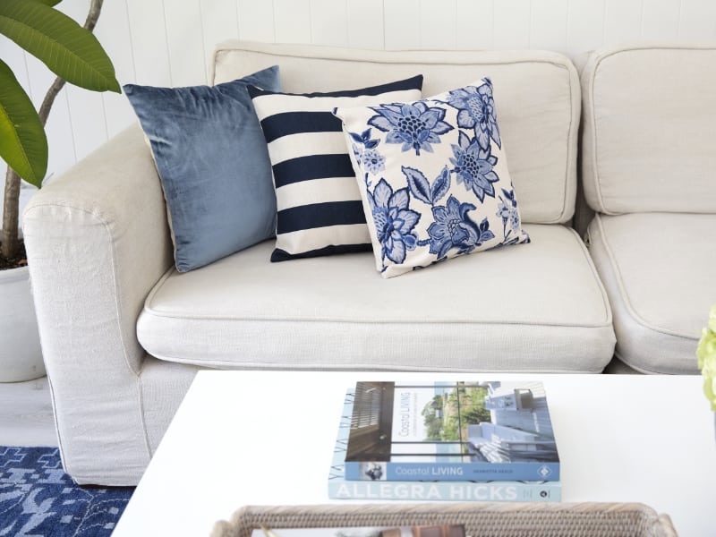 Lovely soft light blue cushions sit on top of each other on a beige couch with books displayed on a nearby coffee table