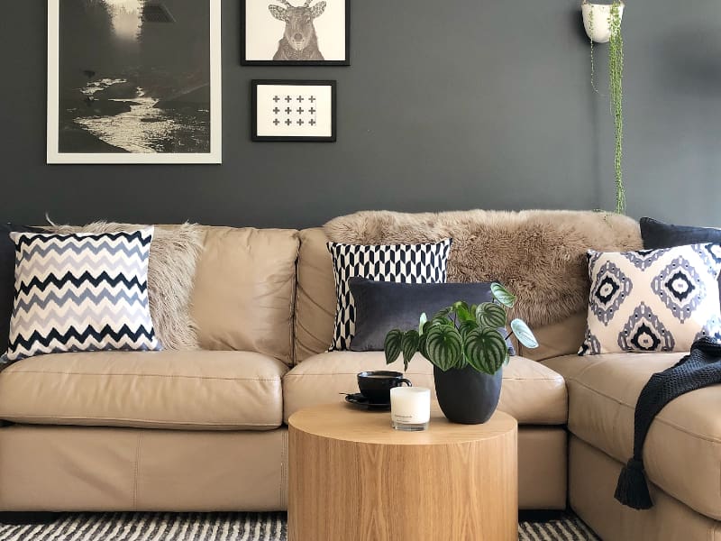 Two grey and white cushions sit within an arrangement on a leather sofa in front of a dark grey wall that features different Scandi influenced artwork 