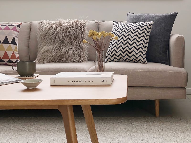 A retro themed living room is shown featuring a light coloured lounge with an arrangement of patterned designs and a grey fluffy cushion