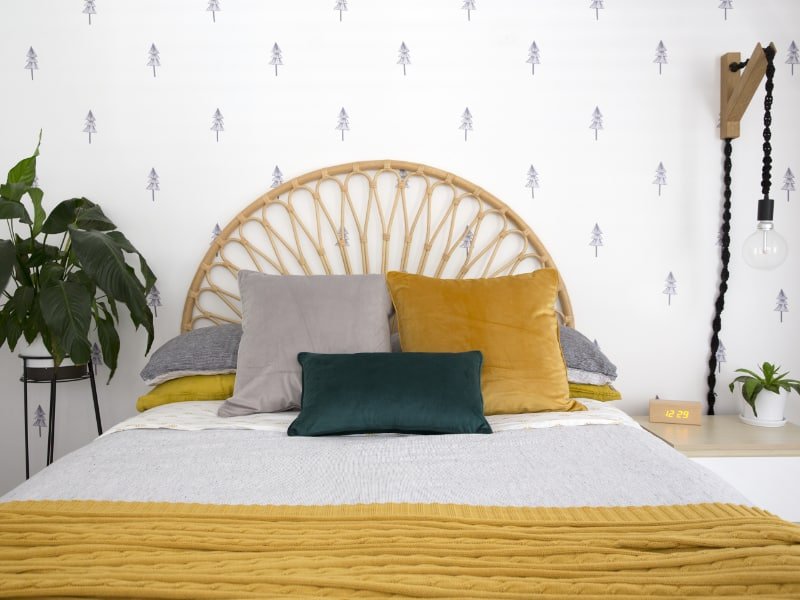 Bright and airy bedroom is shown with a bed styled using mustard cushions and a gorgeous throw