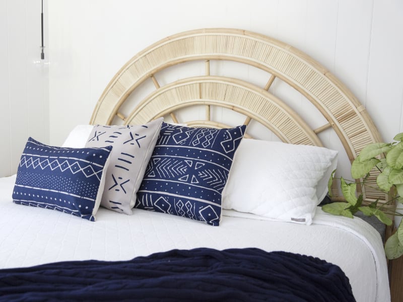 A beautiful bedroom scene is shown with a large bed covered in a white quilt with a selection of navy blue cushions styled in front of the headboard and nearby pillows