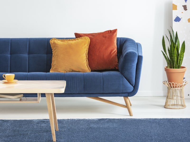 A vibrant living room is shown with a pair of orange cushions displayed on a lovely bright blue sofa with nearby objects like pots and copper coloured decor adding to the rich vibe