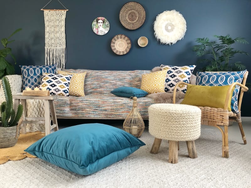 A living room scene is shown with bright teal cushions being partnered with rich mustards that create an interesting and dramatic contrast effect especially against the deep colouring of the back wall
