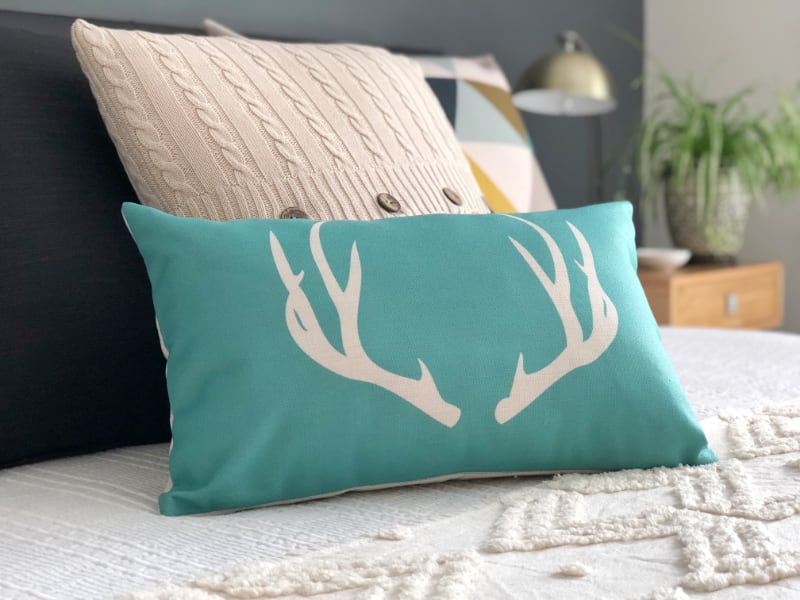 In this picture some stunning turquoise cushions are featured on a white bed cover which has a textured finish and other pillows in the background