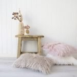 A beautiful rustic room is shown with a small wooden table next to a stack of white fluffy cushion covers