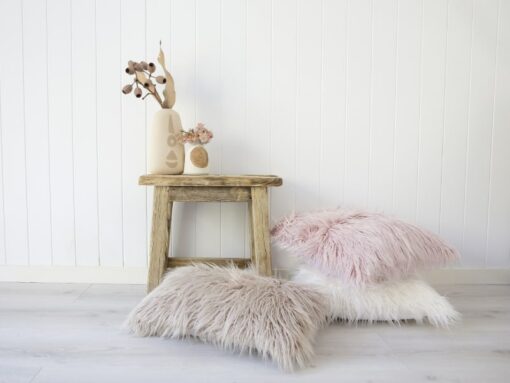 A beautiful rustic room is shown with a small wooden table next to a stack of white fluffy cushion covers