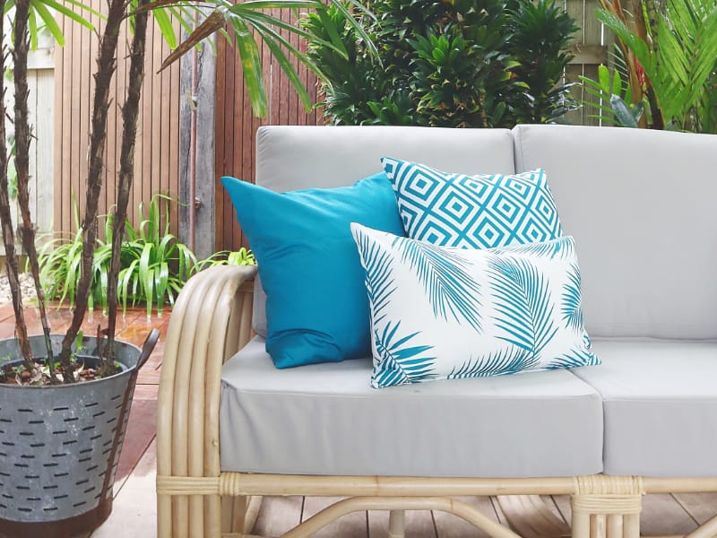 Three aqua cushions site arranged on a grey outdoor sofa in an external living area.