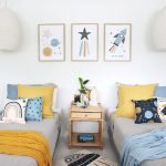 Kids cushions with moon and star prints sitting on two single beds with a mustard throw blanket and a light blue throw. On the wall are three moon and star wall prints that match the cushions