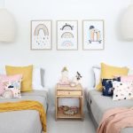 Kids cushions with rainbow prints in blue, pink and navy colours sitting on twin beds with a mustard and pink throw blanket. On the wall are three rainbow kids wall prints that match the cushions