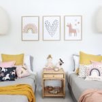 Kids cushions in unicorn pink prints sitting on two single beds with a mustard throw. On the wall are three unicorn prints that match the cushions