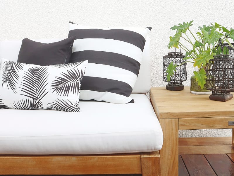 A set of three coordinated black cushions arranged on a wooden outdoor sofa with plants on a side table.