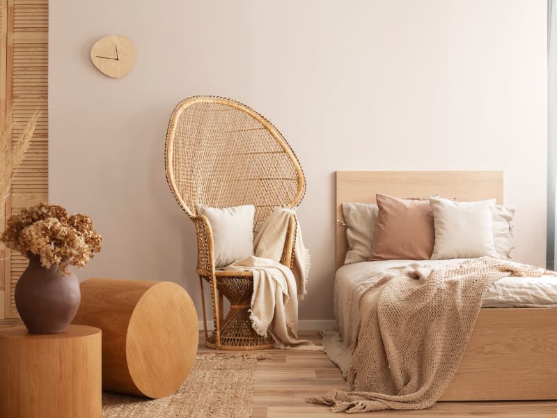 A bedroom scene with a collection of cream cushions arranged on the bed and a nearby tall chair.