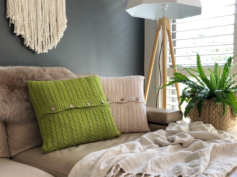 Green and cream knitted cushions lay styled on a leather sofa