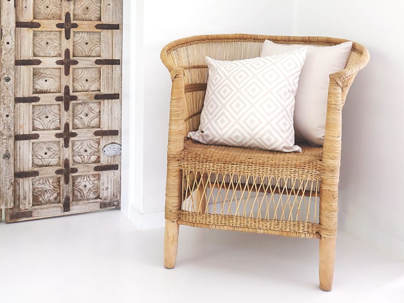 Two outdoor beige cushions are arranged on a woven chair