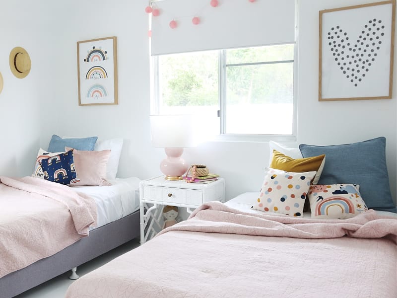 A collection of pink kids cushions with rainbows are shown in a child's bedroom.