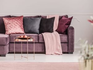 An eclectic mix of pink and purple cushions sit on a purple sofa.