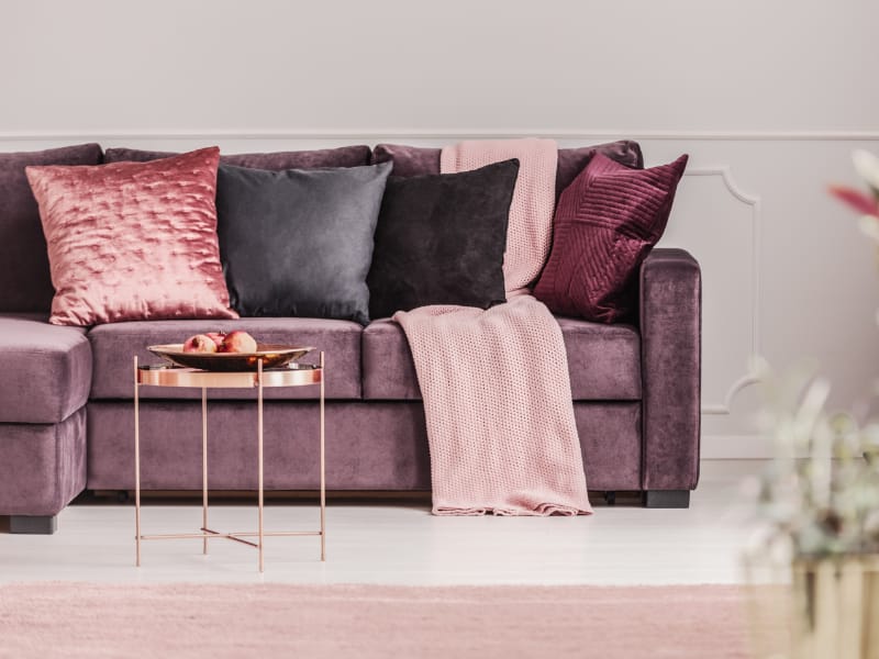 An eclectic mix of pink and purple cushions sit on a purple sofa.