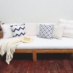 Beige outdoor cushion covers with a highlight of navy and a cream throw blanket on a white outdoor lounge setting