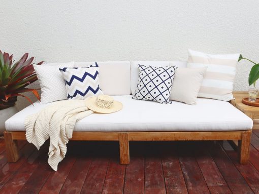 Beige outdoor cushion covers with a highlight of navy and a cream throw blanket on a white outdoor lounge setting