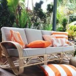 Orange outdoor cushion covers on a light grey three seater outdoor setting with a striped orange and white floor cushion