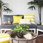 Bright yellow outdoor cushions on a dark grey outdoor 2 seater chair with a yellow striped outdoor floor cushion