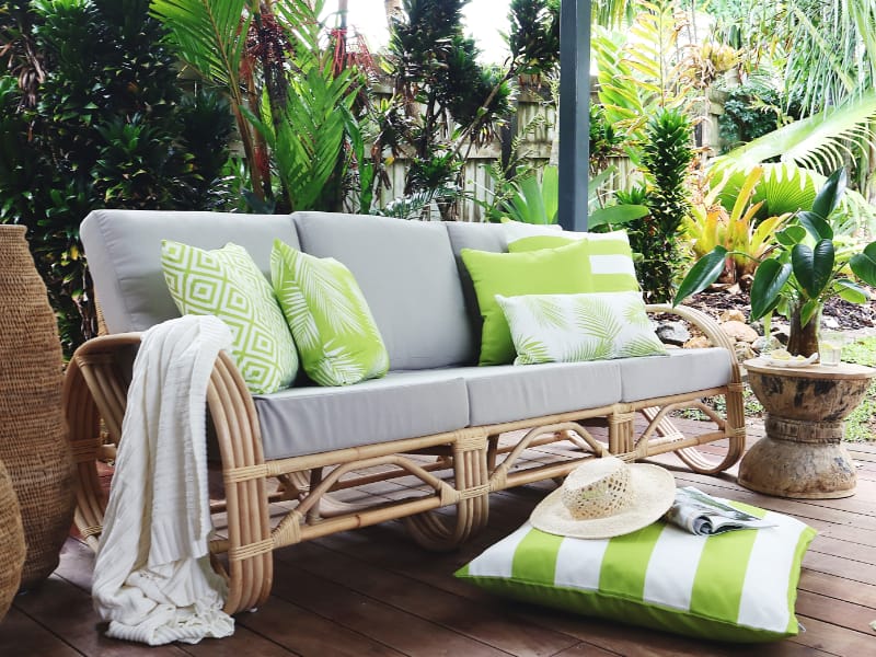 A grey sofa has five green outdoor cushions that are large in size styled on it with a throw.