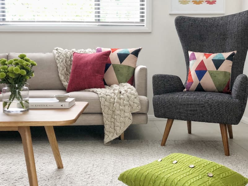 A collection of retro cushions sit on a light sofa in a funky living room with mid century decor.