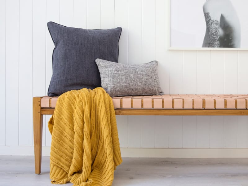 Mustard throw blankets styled on a bench with grey cushions nearby.
