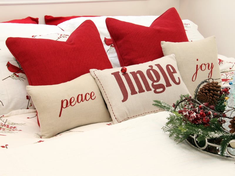Red and white Christmas cushions are arranged on a white bed