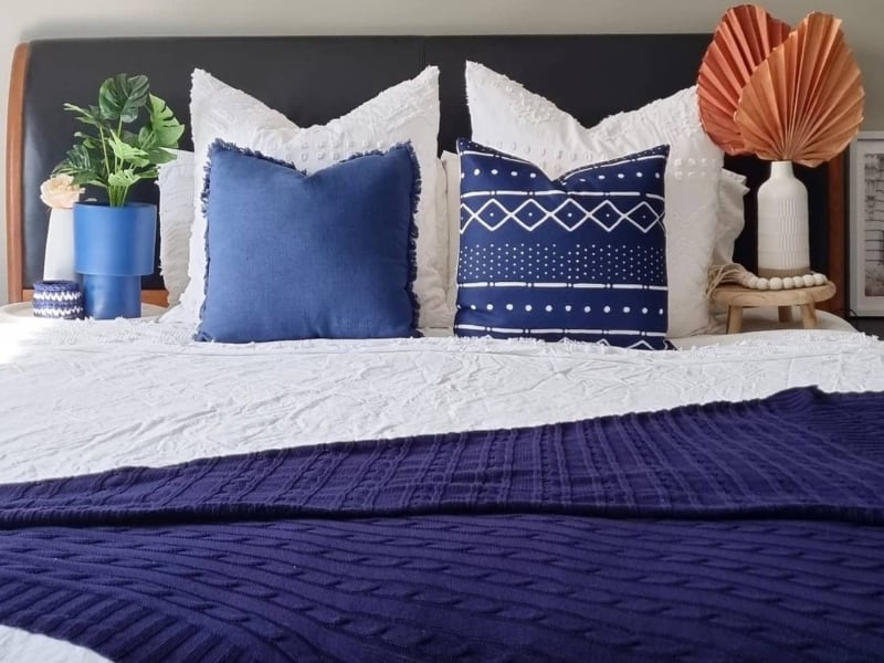 Navy blue throw blanket styled on a white bed with blue cushions.